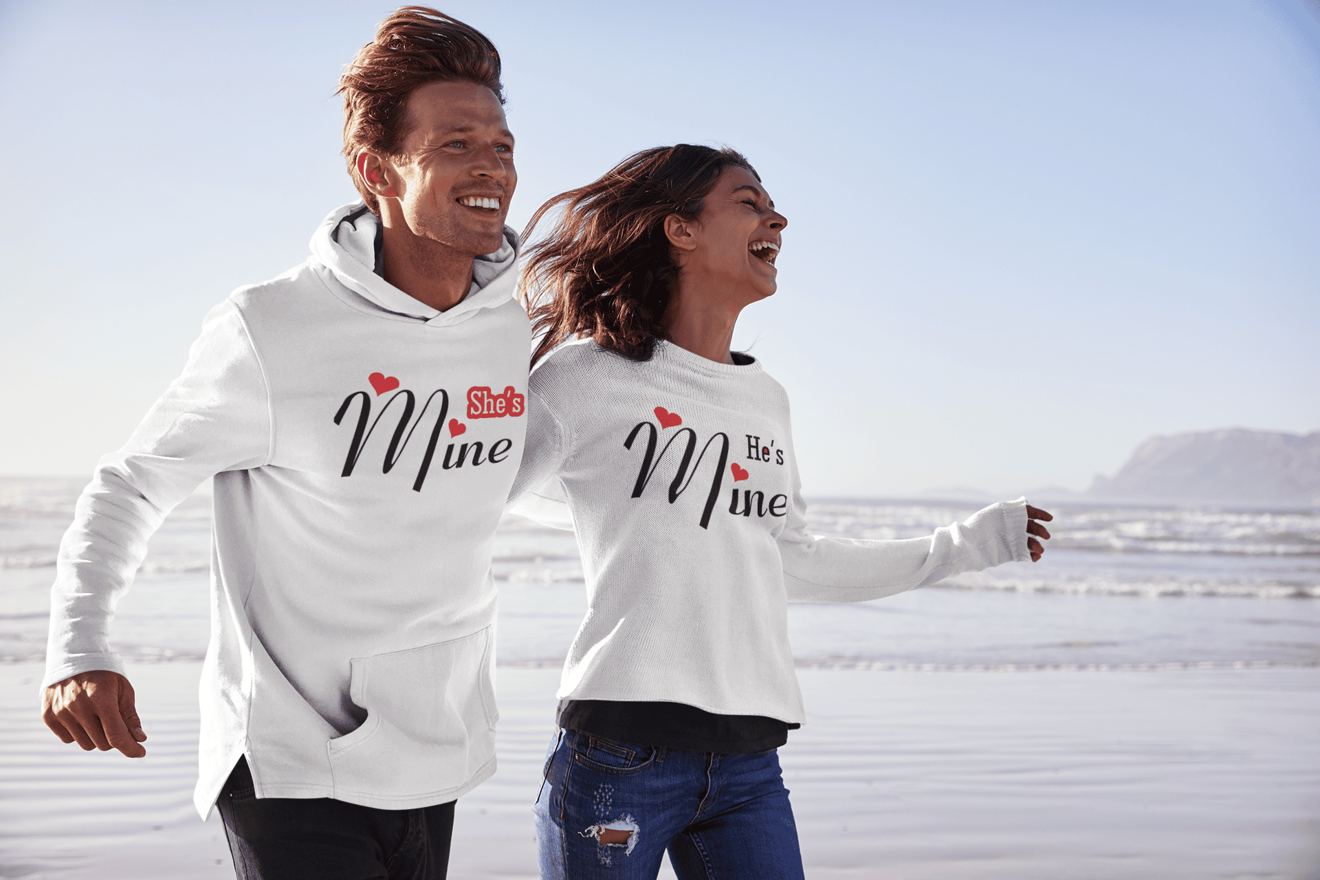 Couple laughs on beach wearing Shes Mine, Hes Mine matching shirts.